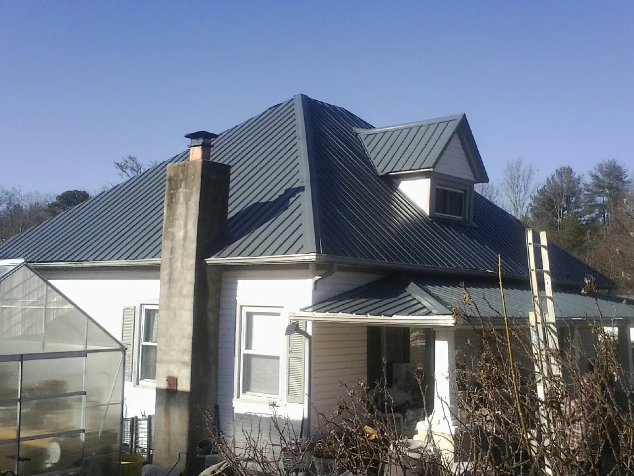 Dark blue standing seam metal roof on a white farmhouse with dormer — Slate & Tile Roof Repair by Roofing Brothers in Bronwood
