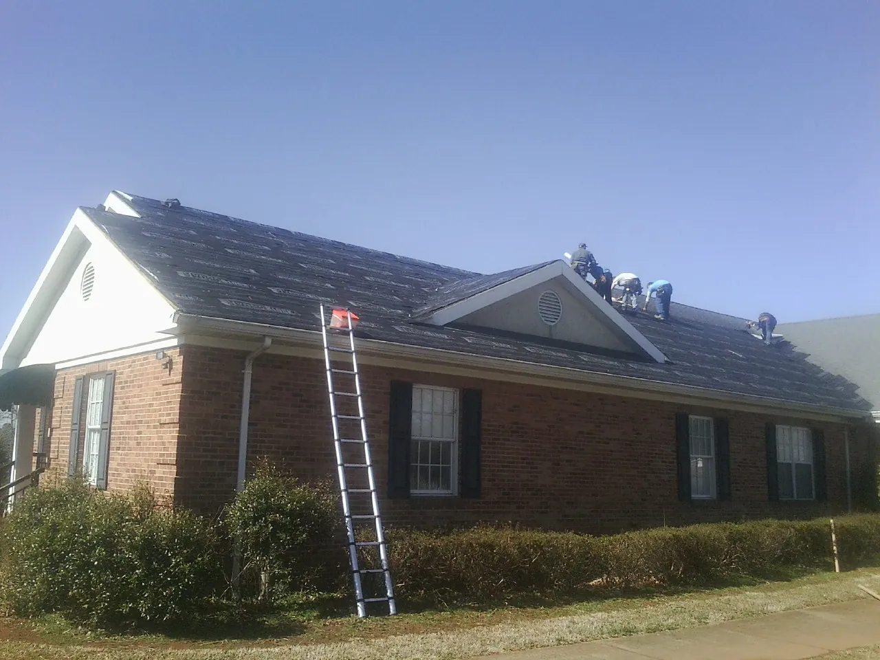 Crew tearing shingles off a brick ranch roof with a ladder set — Metal Roof Repair work by our crew in Bronwood