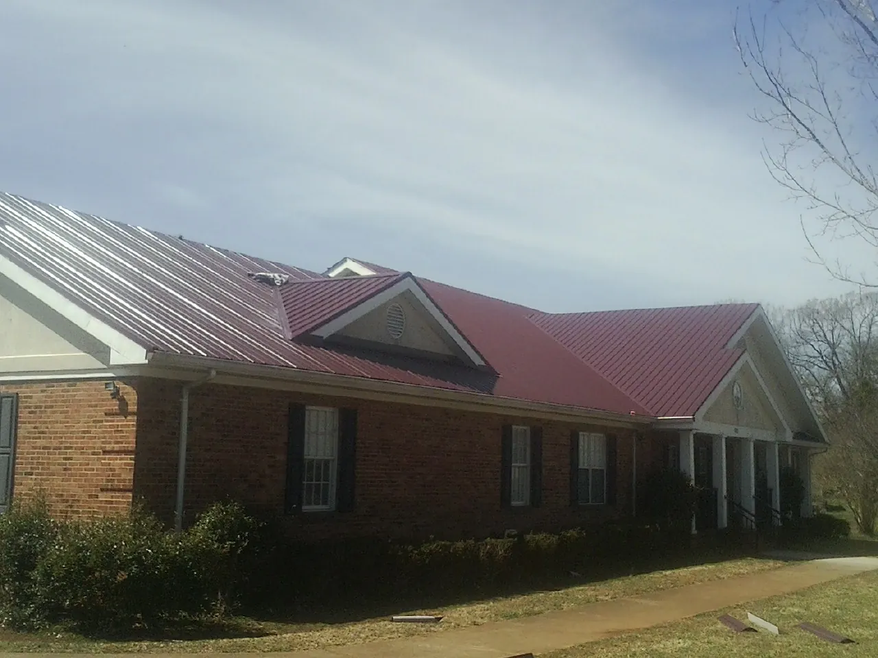 Red metal roof with gabled entries on a long brick building, from a Hail Damage Roof Repair job in Bronwood