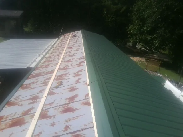 Old rusted panels beside newly installed green metal roofing — Wind Damage Roof Repair by Roofing Brothers in Bronwood