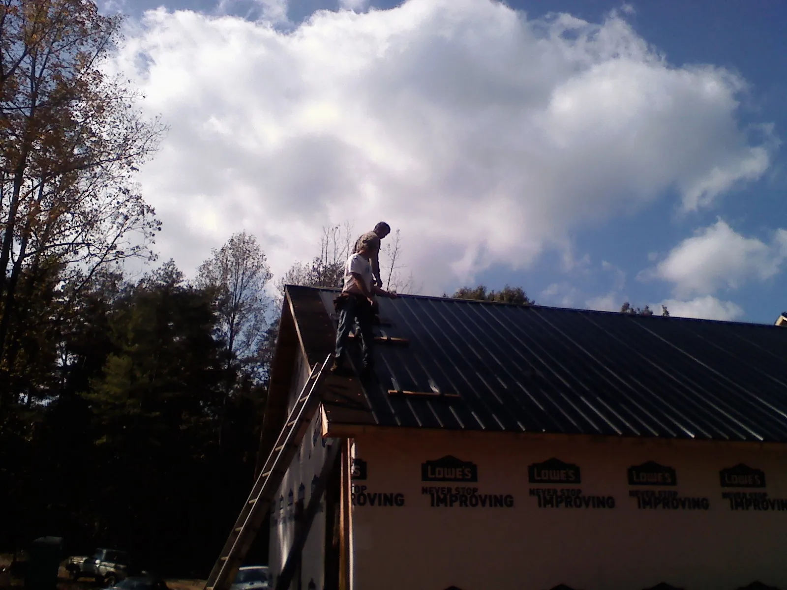 Roofer fastening dark metal panels high against a cloudy sky, from a Roof Inspection job in Bronwood