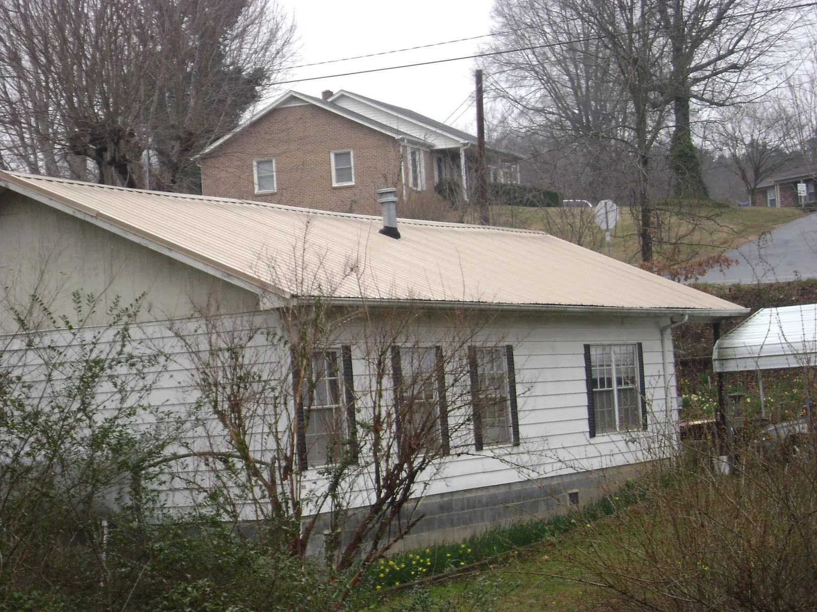 Tan metal roof on a white sided house set into a hillside — Commercial Roofing by Roofing Brothers in Bronwood